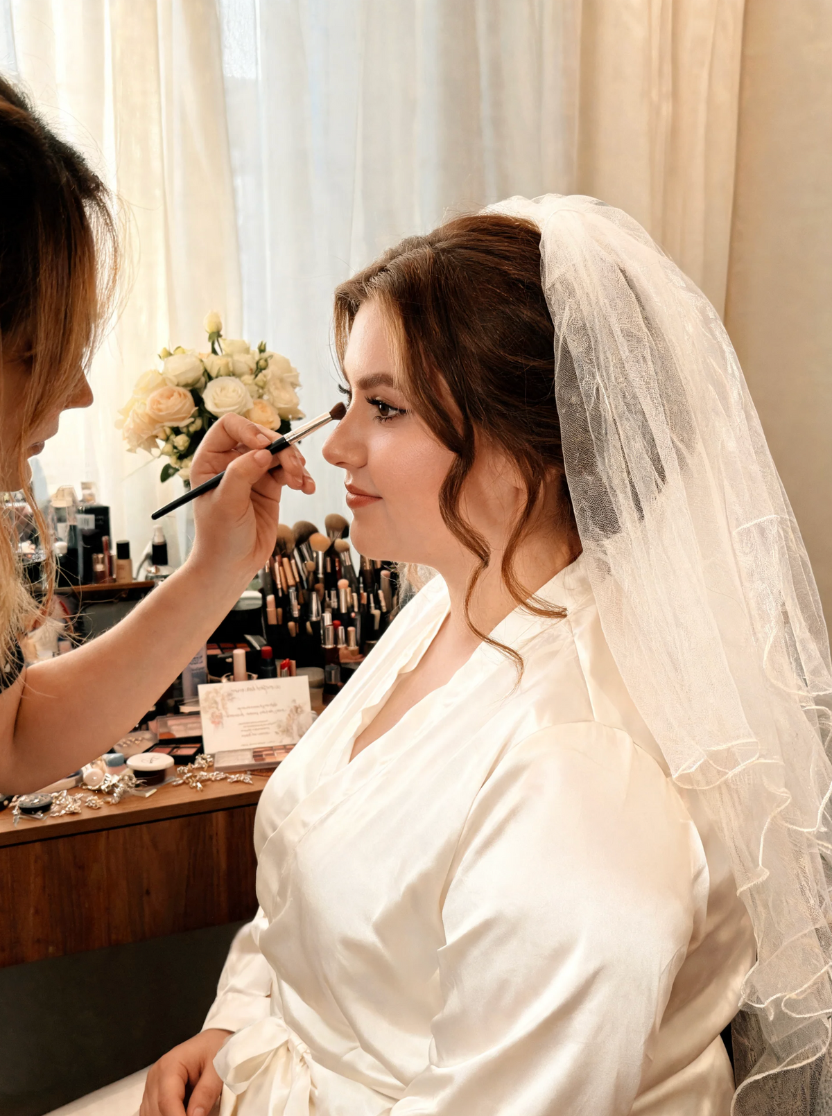 Bride in a lace-edged veil having her makeup done before the ceremony