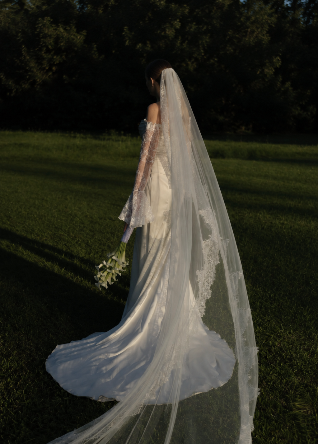 Bride in a long tulle veil on a lawn at dusk