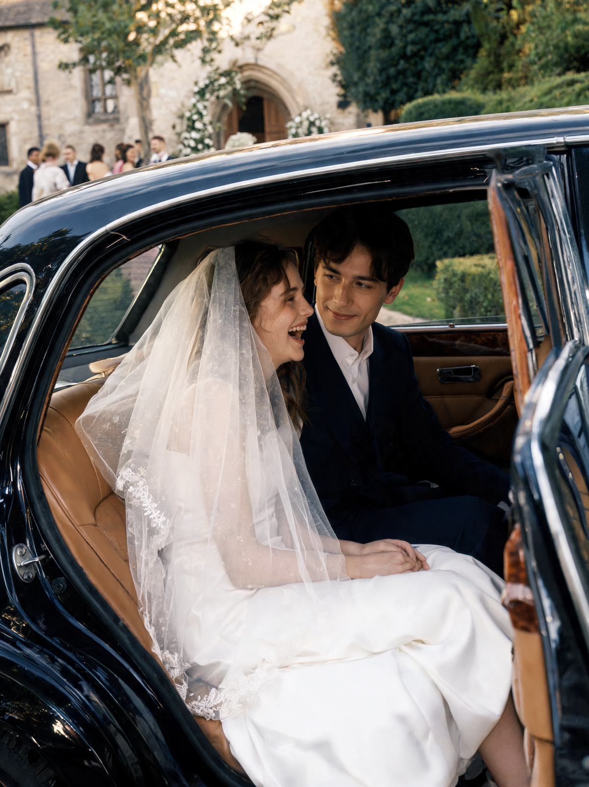 Bride in a long tulle veil sitting with the groom in a vintage car